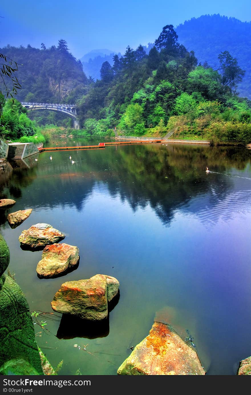 A beautifuk lake with stepping stones from the Wudang Shan mountain in the Hubei district in China. Lush vegetation and mountains in the background. A beautifuk lake with stepping stones from the Wudang Shan mountain in the Hubei district in China. Lush vegetation and mountains in the background.