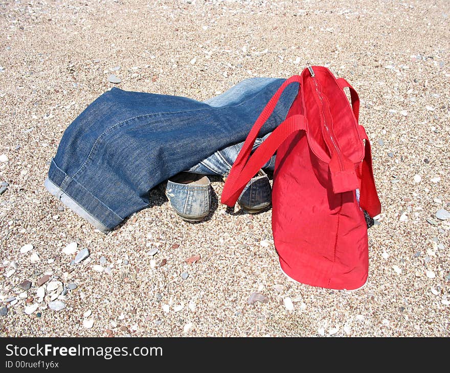 There are jeans, shoes and a bag on the beach. There are jeans, shoes and a bag on the beach