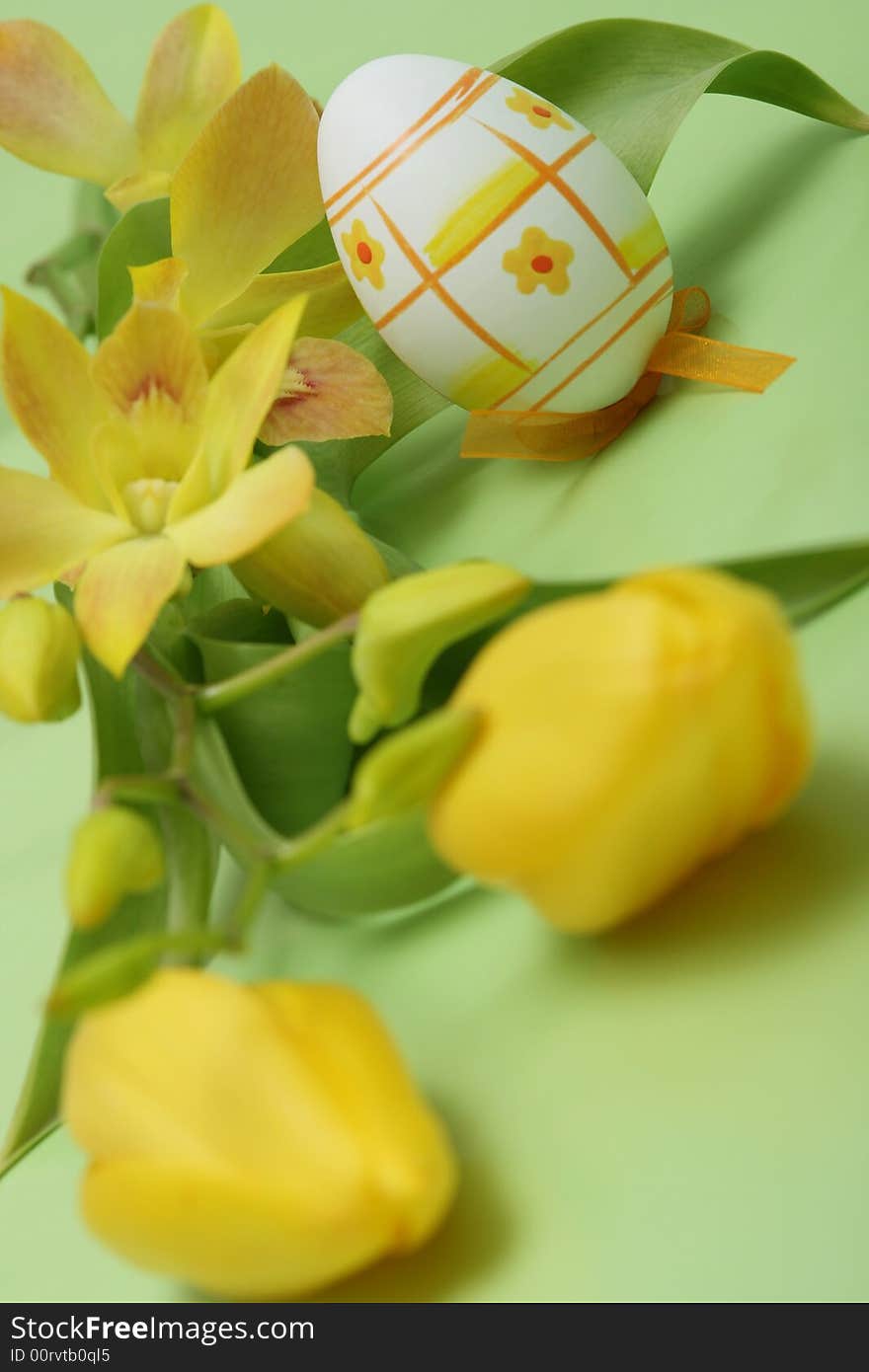 Easter egg with yellow tulip and yellow orchid on green background.