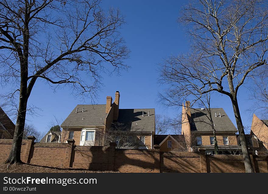 Large brick houses against a blue sky with bare winter trees and a brick wall. Large brick houses against a blue sky with bare winter trees and a brick wall