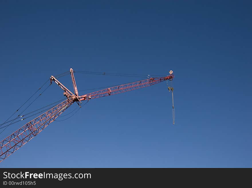 A red crane against a blue sky with a pulley attached. A red crane against a blue sky with a pulley attached