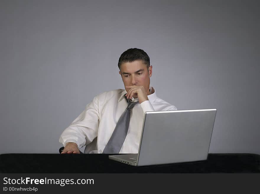 A professional business man in suit and tie sits on office chair looking seriously away from computer. A professional business man in suit and tie sits on office chair looking seriously away from computer.