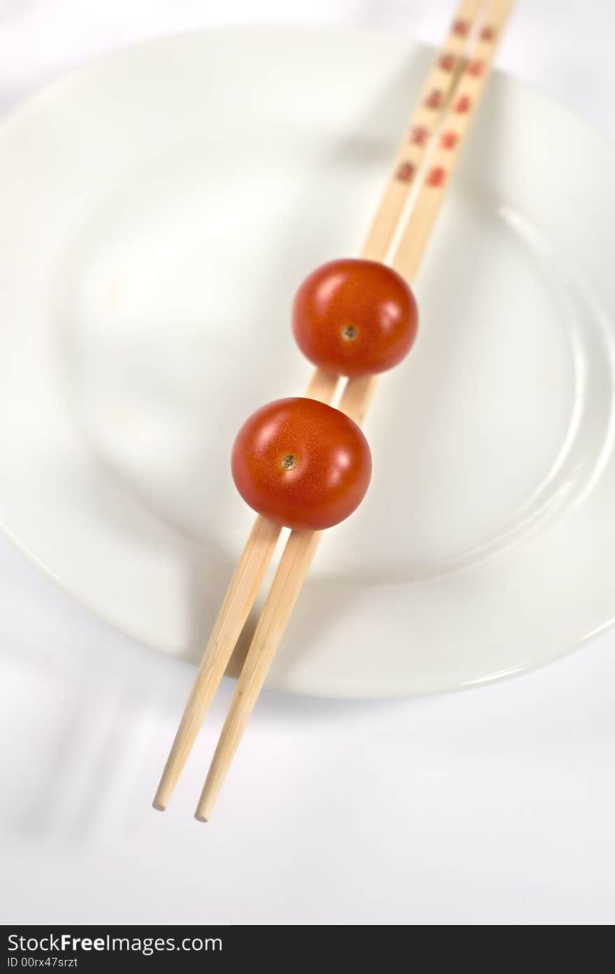 Three cherry tomatoes on a white plate with chopsticks. Three cherry tomatoes on a white plate with chopsticks