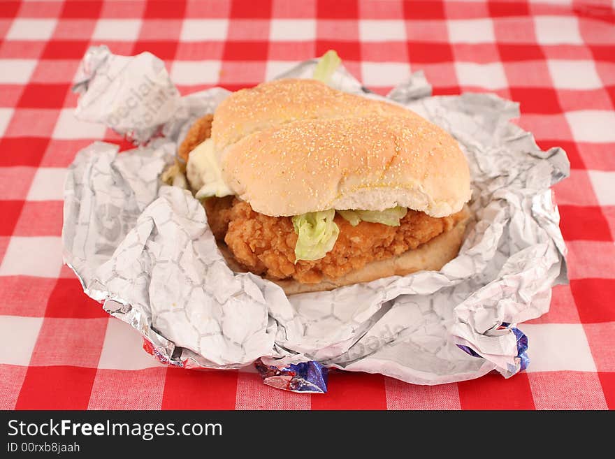 Fast food crispy chicken burger still in wrapper with checkered red background