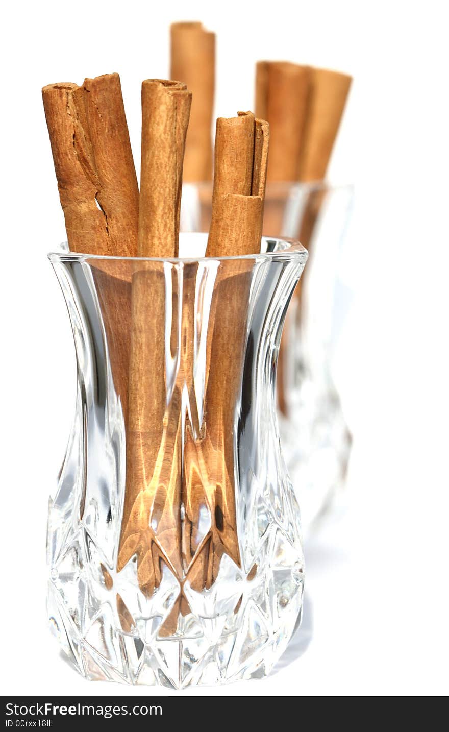 Cinnamon sticks in crystal glass and second one on background, light shadow. Cinnamon sticks in crystal glass and second one on background, light shadow