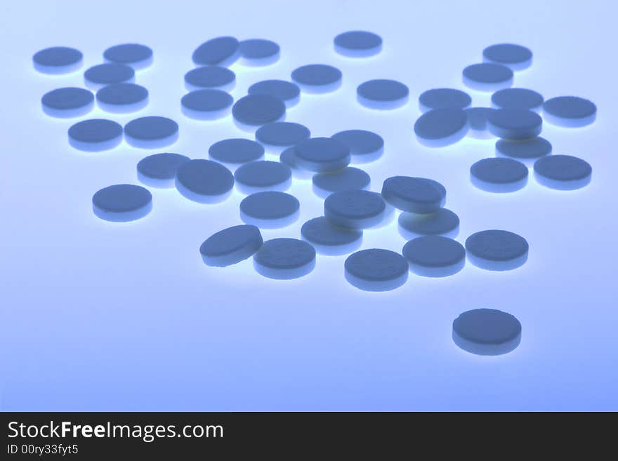 Back-lit close-up of blue toned vitamin pills against a plain background