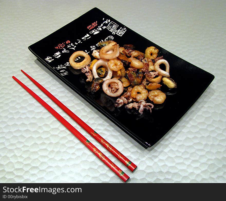 Black square plate with red sticks and sea food. Black square plate with red sticks and sea food