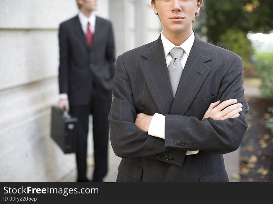 Two businessmen standing in front of building wearing suits looking at camera. Two businessmen standing in front of building wearing suits looking at camera