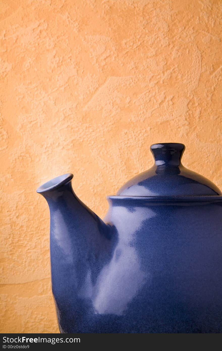 Blue ceramic teapot in front of wall.