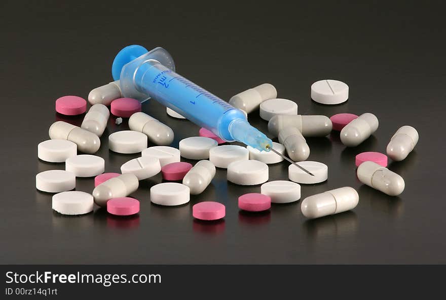 Blue syringe with tablets and pills isolated on a black background. Blue syringe with tablets and pills isolated on a black background