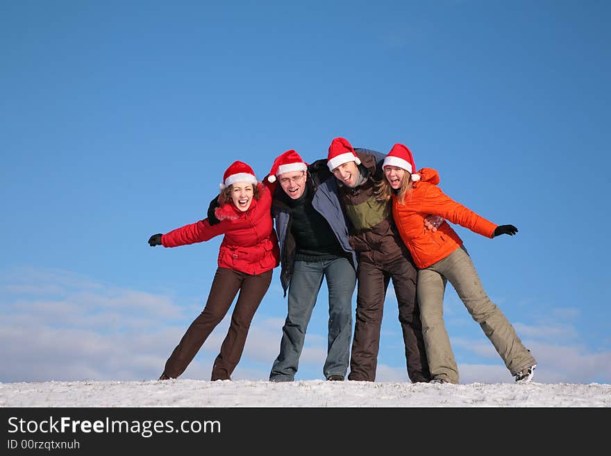 Four friends embracing on top of snow hill in santa claus hats. Four friends embracing on top of snow hill in santa claus hats