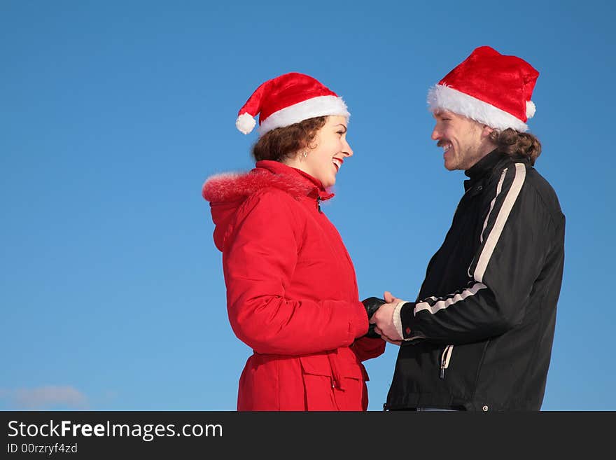 Couple against blue sky background in winter in santa claus hats stand face to face