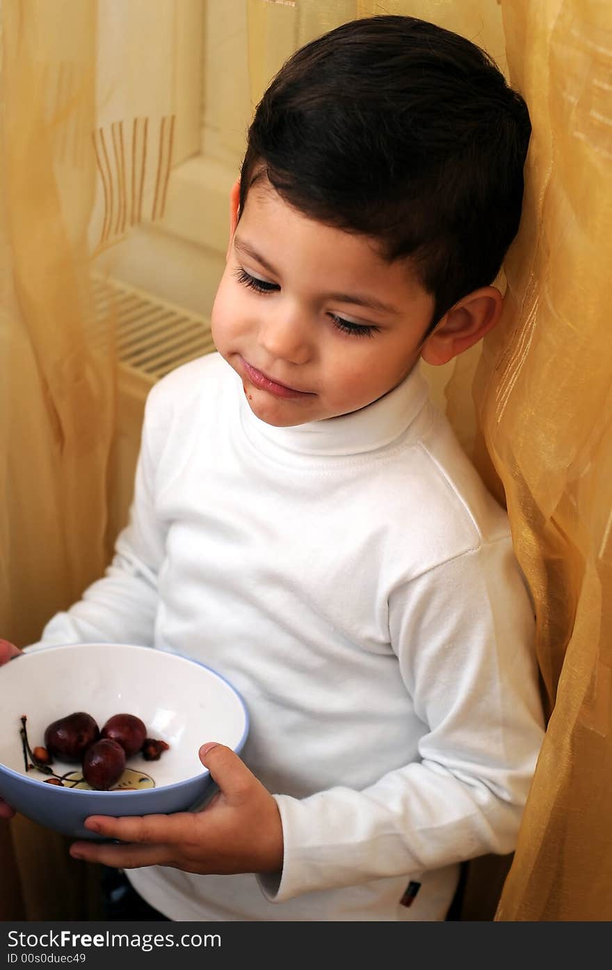 A view with a little boy eating cherries from a bowl