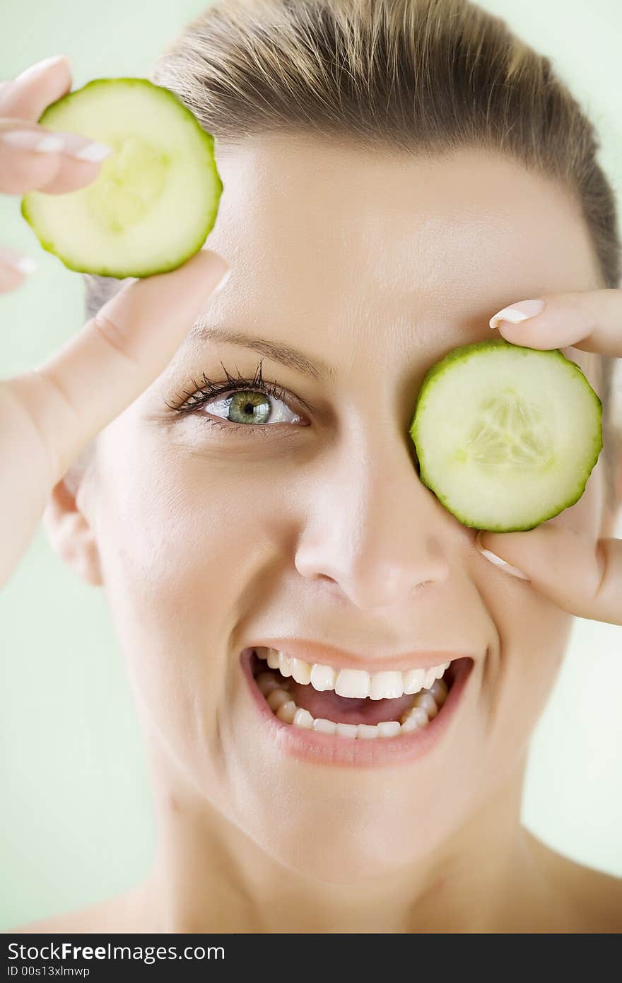 Smiling woman holding cucumber-slices in front of her eye. Smiling woman holding cucumber-slices in front of her eye