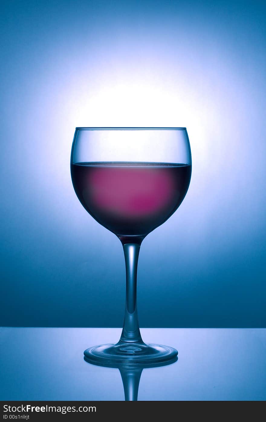 Image of a glass of dark wine silhouetted against a blue spotlight on dark background with reflection. Image of a glass of dark wine silhouetted against a blue spotlight on dark background with reflection