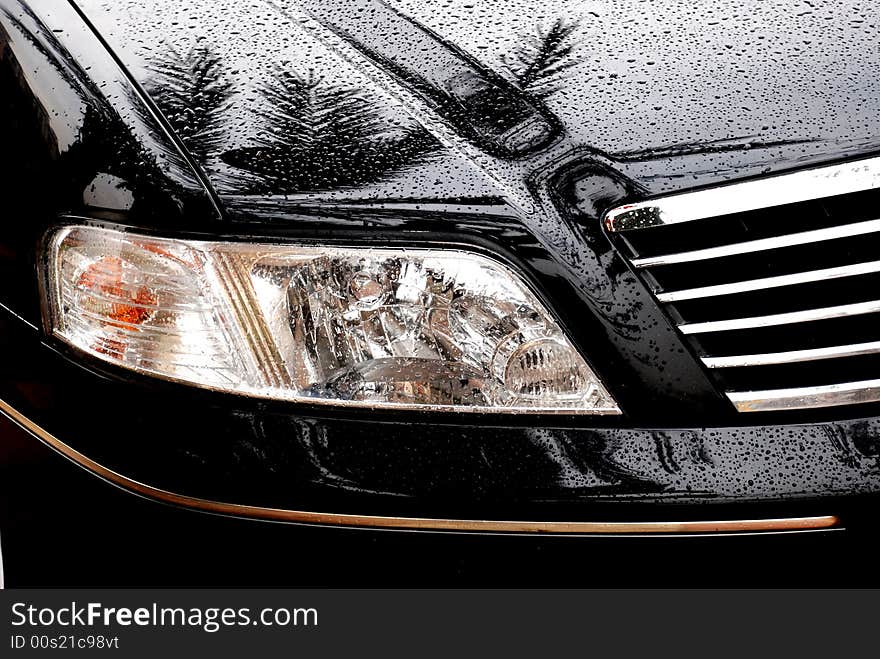 The headlight of a black car in the rain,with raindrops on the hood. The headlight of a black car in the rain,with raindrops on the hood