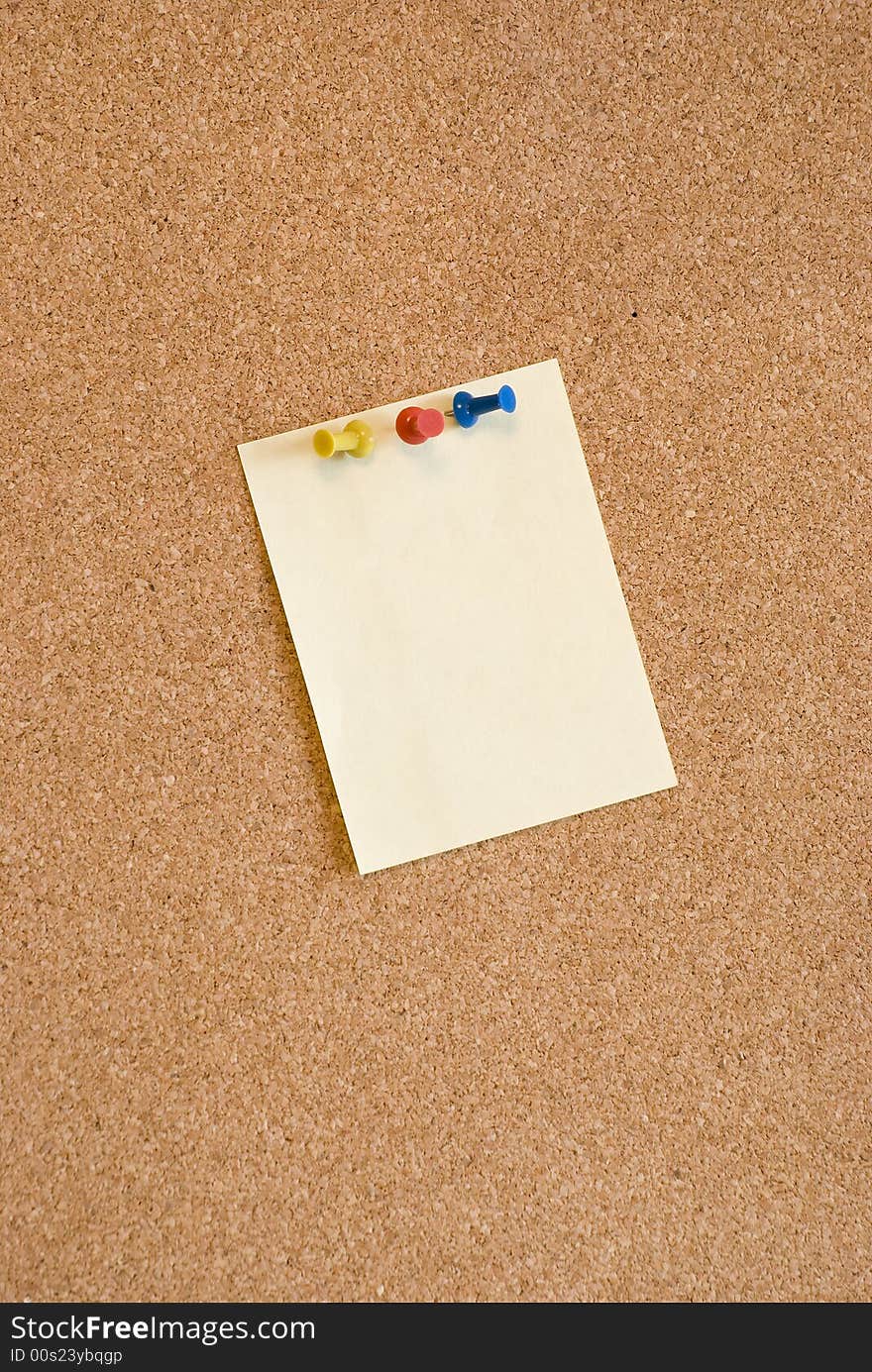 A close-up of a note page is attached to the board with blue, yellow and red pins. A close-up of a note page is attached to the board with blue, yellow and red pins