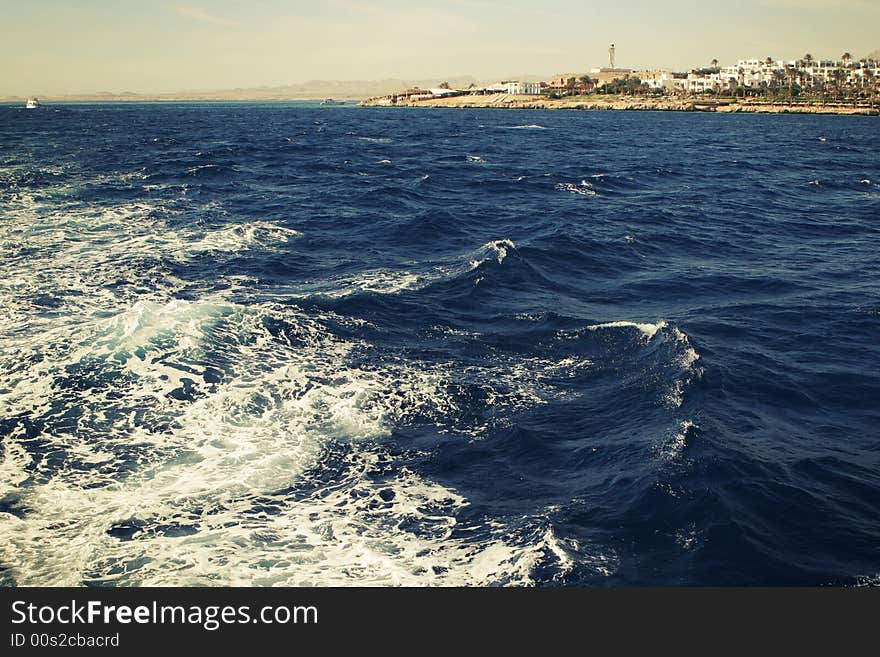 Dark blue sea with foam and short view to the coast