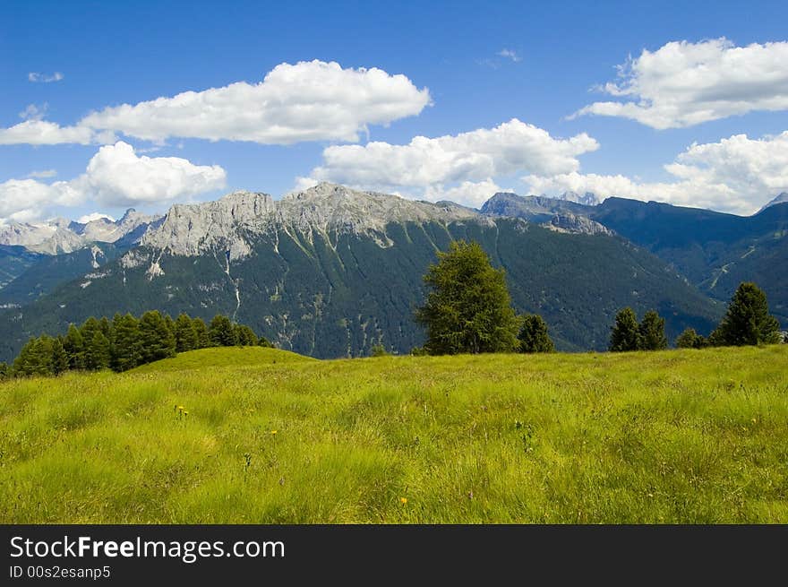 View of dolomites mountains with green gras, blue sky and white clouds