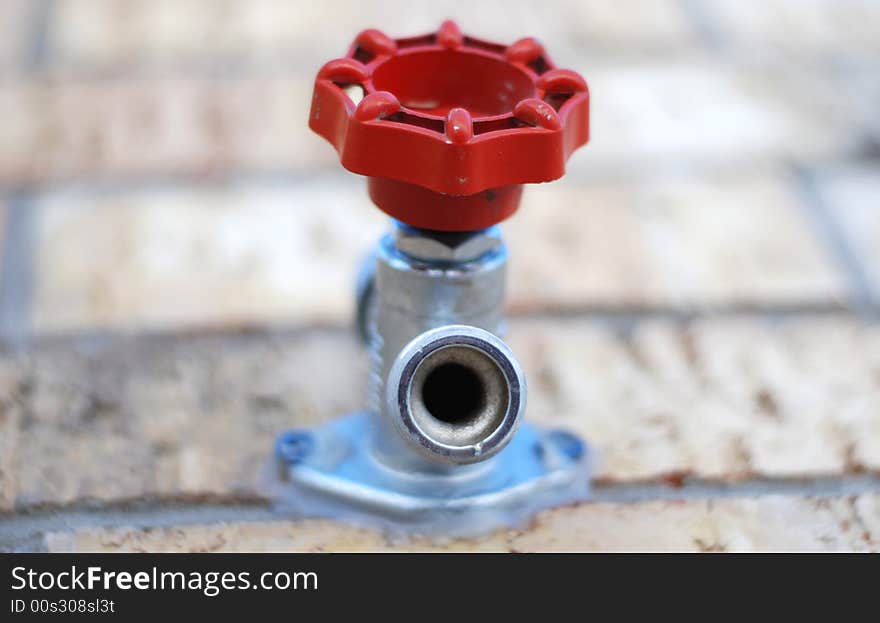 Outdoor water spigot with a red handle attached to a brick wall. Shallow DOF