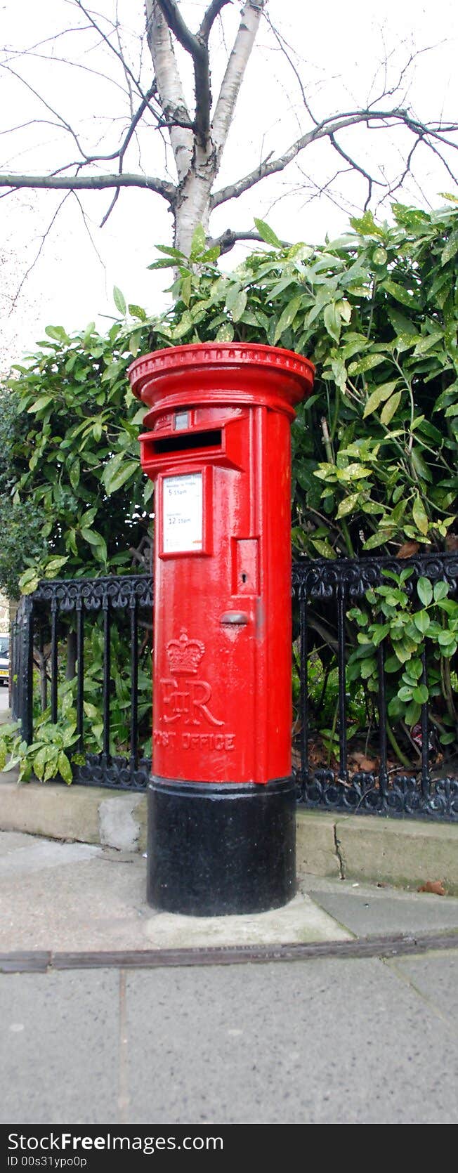 Bright red British pillar box against background of evergreen leaves . Bright red British pillar box against background of evergreen leaves