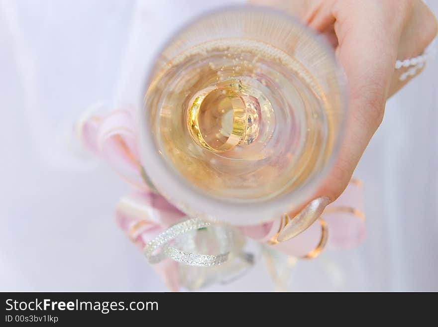 A hand of a bride holds a glass full of champagne and two gold rings in it. A hand of a bride holds a glass full of champagne and two gold rings in it