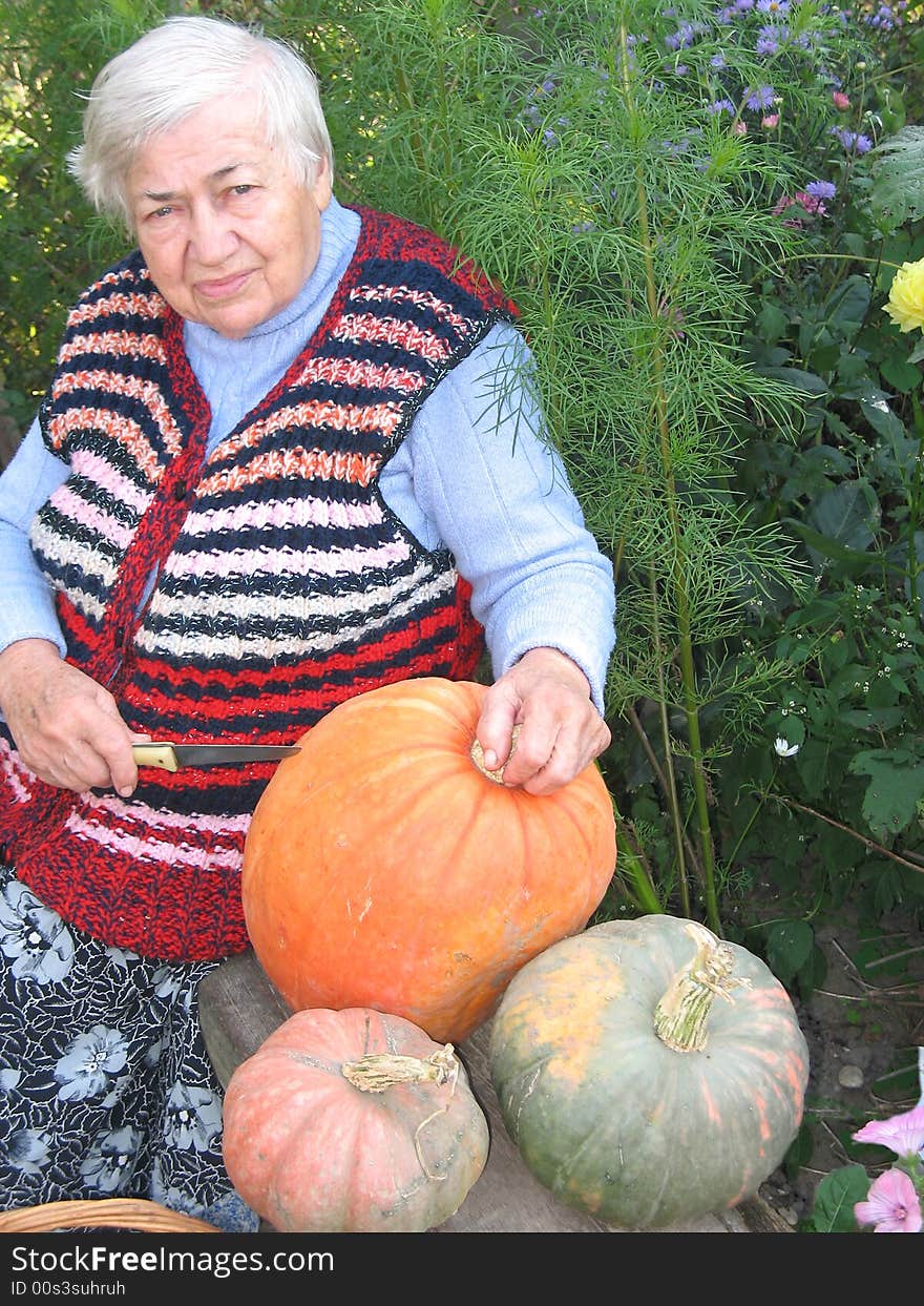 The old woman is sitting on the bench and cutting the pumpkins. The old woman is sitting on the bench and cutting the pumpkins