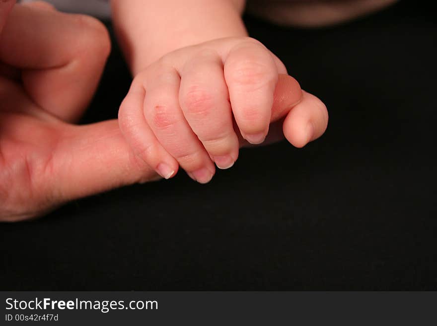 A newborn grasps her mother's finger tightly. There is room to the bottom right of the subject for text. A newborn grasps her mother's finger tightly. There is room to the bottom right of the subject for text.