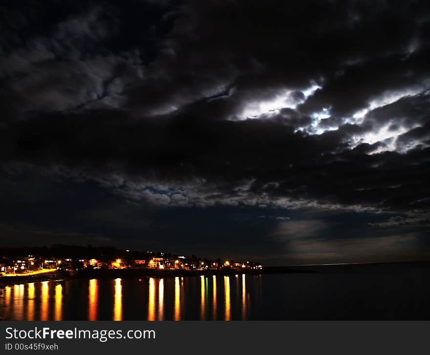 A harbour with a bright moon in the sky.  Homes and houses across the bay. A harbour with a bright moon in the sky.  Homes and houses across the bay.