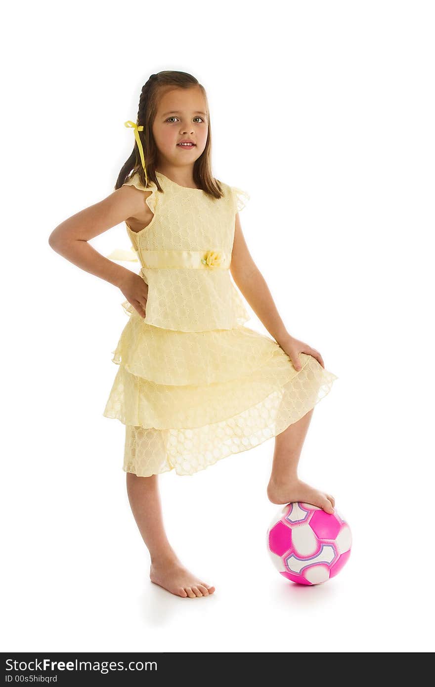 Little girl in a pretty yellow dress with her bare foot on a pink soccer ball. One of series. Studio shot isolated on a white background. Little girl in a pretty yellow dress with her bare foot on a pink soccer ball. One of series. Studio shot isolated on a white background.