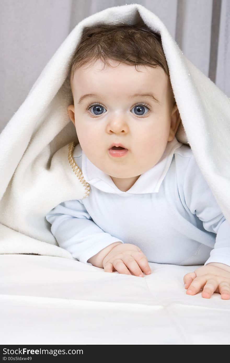 The little boy of 7 months looks out from under coverlets.