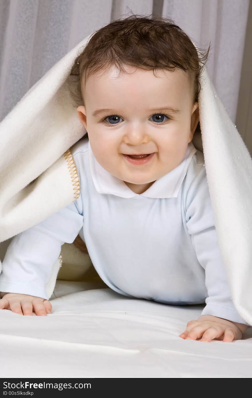 The little boy of 7 months looks out from under coverlets.