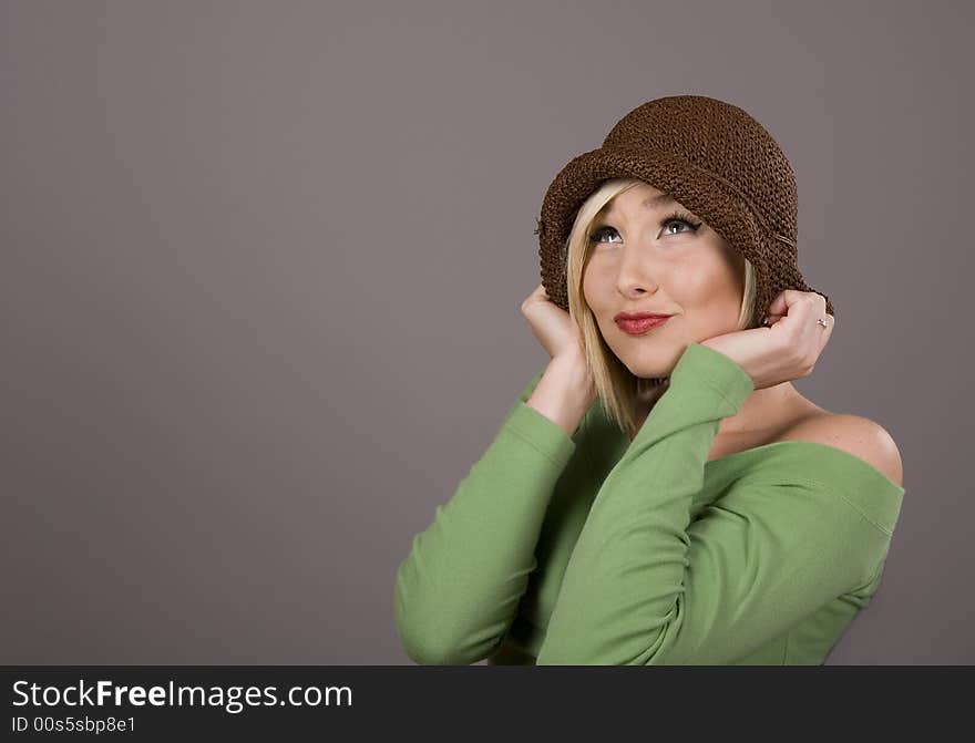 A blonde model in brown hat and green blouse looking up against grey background. A blonde model in brown hat and green blouse looking up against grey background