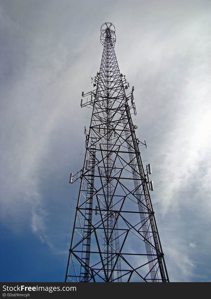 This is a transmitting and receiving tower against a whispy cloud type blue sky. This is a transmitting and receiving tower against a whispy cloud type blue sky