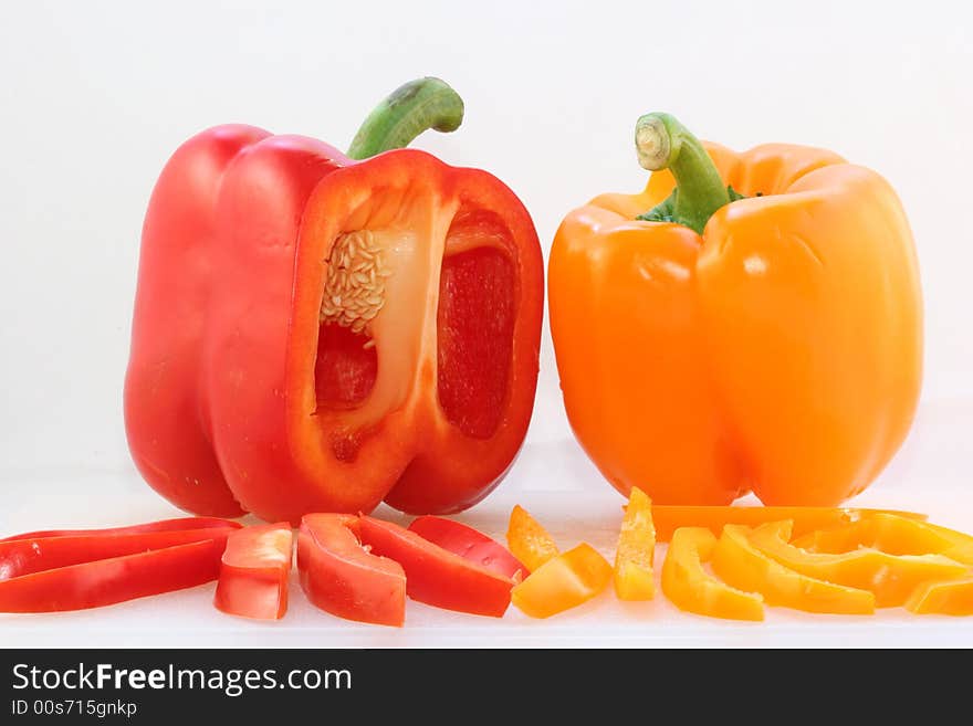 A red and a yellow bell pepper on a white cutting board with fresh cut slices in front. Isolated on a white background. A red and a yellow bell pepper on a white cutting board with fresh cut slices in front. Isolated on a white background.