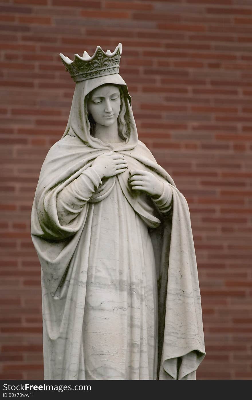 Angel statue with crown in front of red brick wall.