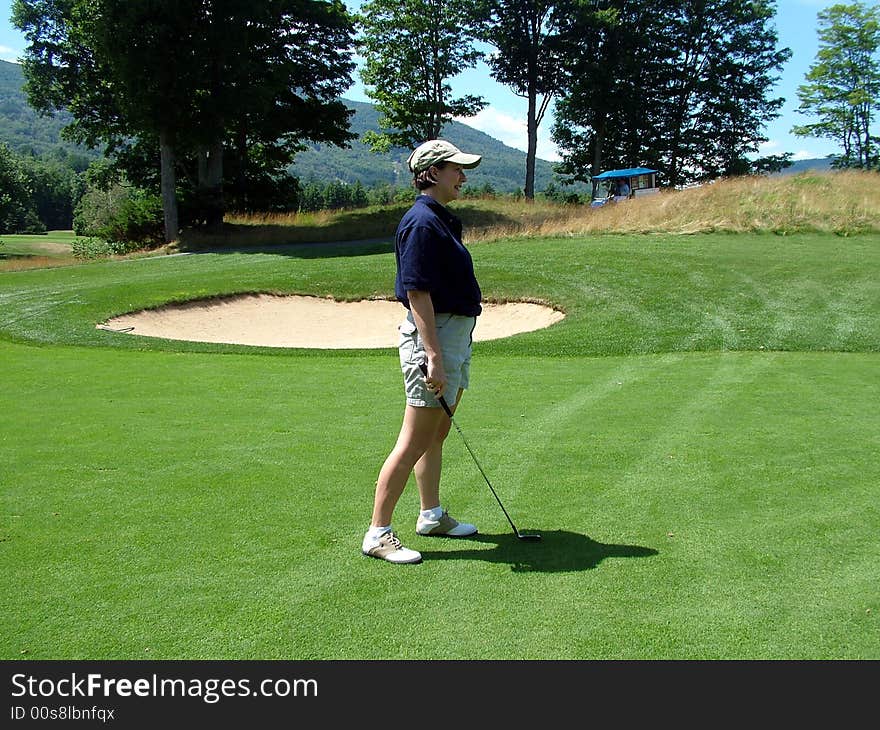 A lady golfer looks on as her golf ball approaches the hole. A lady golfer looks on as her golf ball approaches the hole.