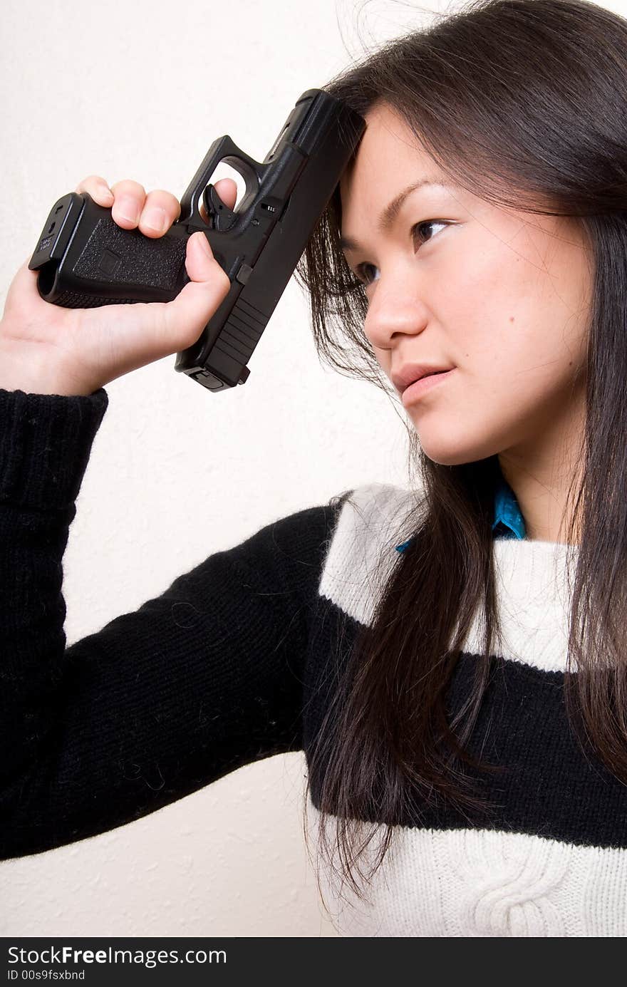 An Asian female resting a tip of a gun on her head as if she is thinking about something bad. An Asian female resting a tip of a gun on her head as if she is thinking about something bad.