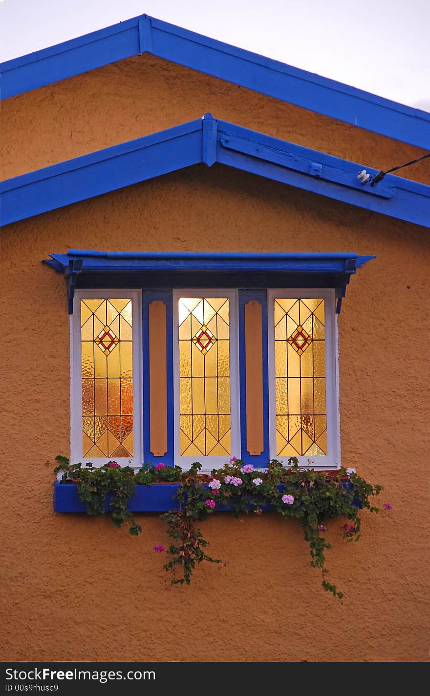 The light is shining out through the leadlight window of a small cottage. The light is shining out through the leadlight window of a small cottage