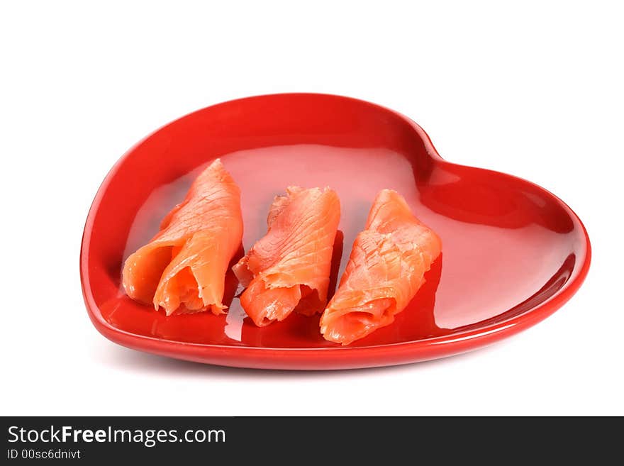 Three pieces of smoked salmon on red heart shape plate, white background, light shadow