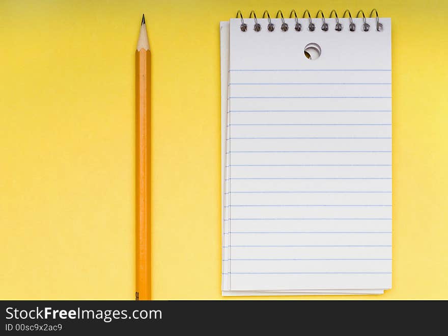 Pencil and blank notebook on yellow