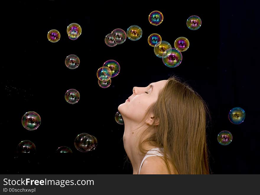 The teenage girl and soap-bubbles on the black background