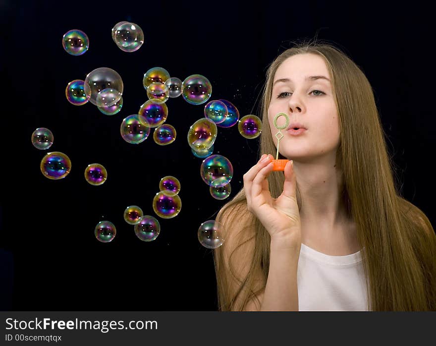 The teenage girl is blowing soap-bubbles on the black background