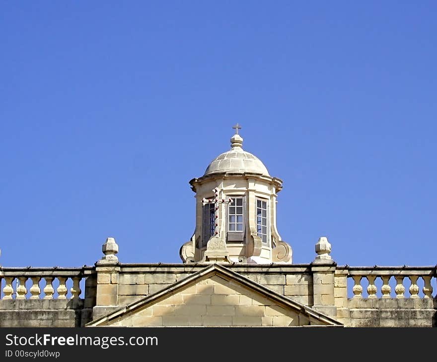 A traditional Maltese church top against clear blue sky.