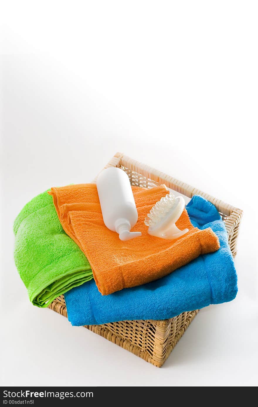 Mixed color bath towels, massager and lotion bottle in a square basket isolated on white background. Mixed color bath towels, massager and lotion bottle in a square basket isolated on white background.