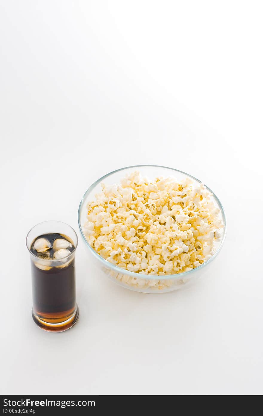 A glass bowl full with popcorn and a glass of cola with ice cubes isolated on white background. A glass bowl full with popcorn and a glass of cola with ice cubes isolated on white background.