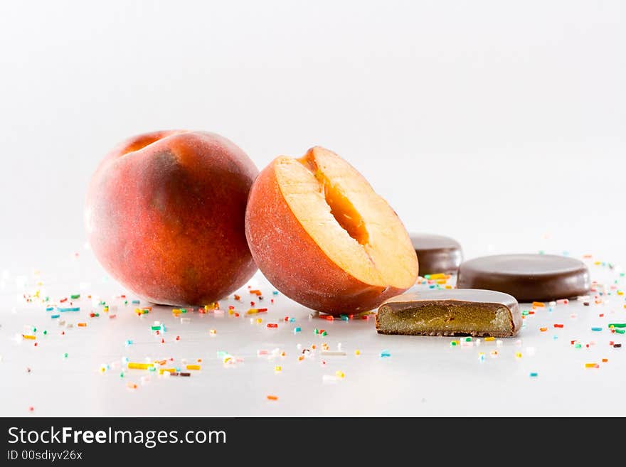 Whole and half peach, cream filled chocolate and sugar confetti on white background. Whole and half peach, cream filled chocolate and sugar confetti on white background.