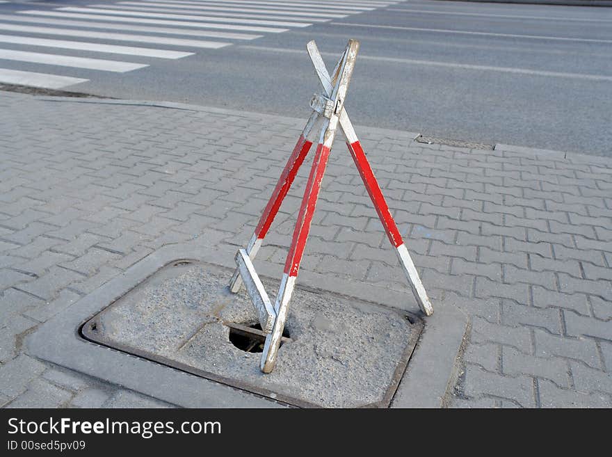 Wooden road tripod barrier placed over hole in sidewalk to protect pedestrians from falling into it