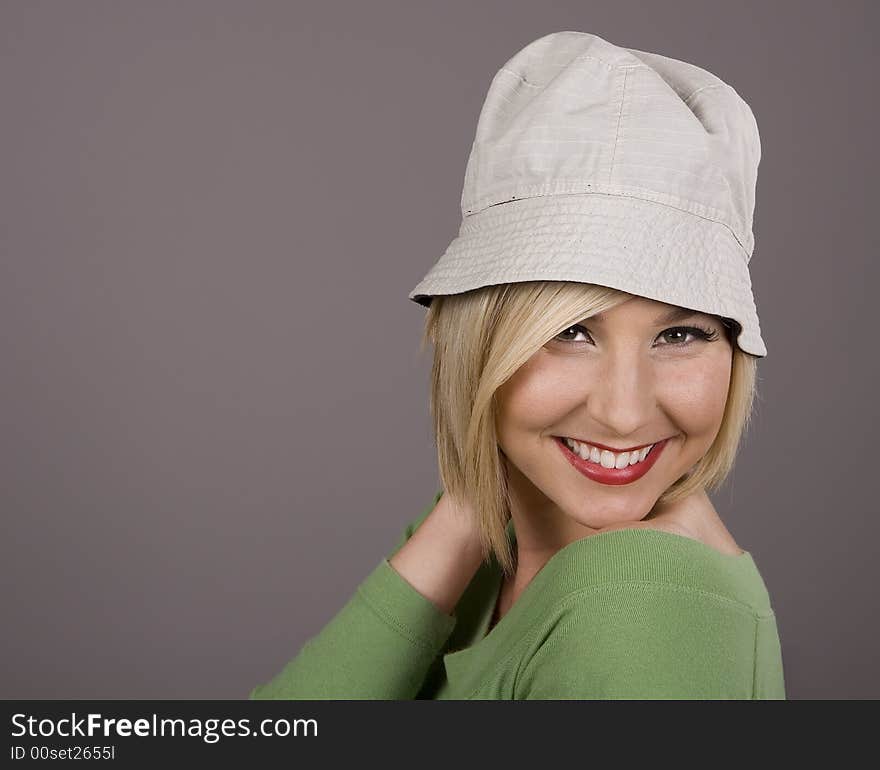 A blonde in a green blouse and silly white hat smiling with her hand behind her head. A blonde in a green blouse and silly white hat smiling with her hand behind her head