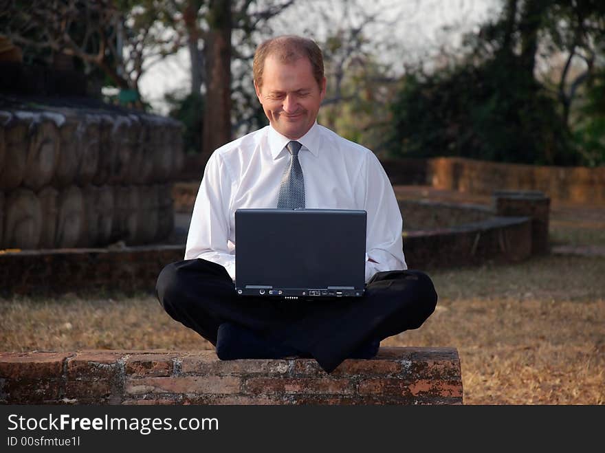 A middle aged man working on a computer in a park. A middle aged man working on a computer in a park